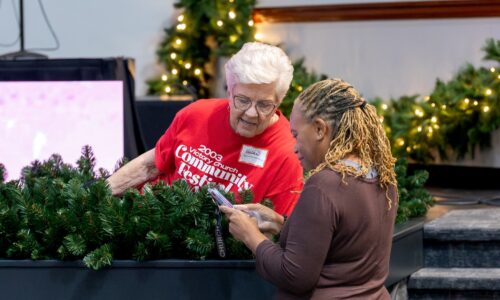 Two Victory Church volunteers smiling and working together while decorating with greenery and Christmas lights